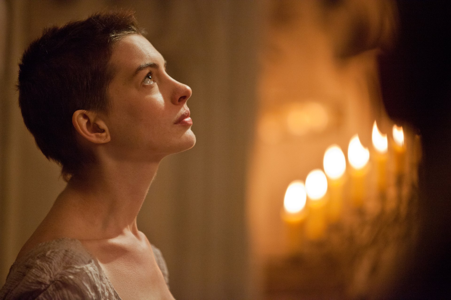 HD desktop wallpaper featuring Anne Hathaway from the 2012 movie Les Misérables, showcasing her character with a contemplative expression and soft candlelight in the background.