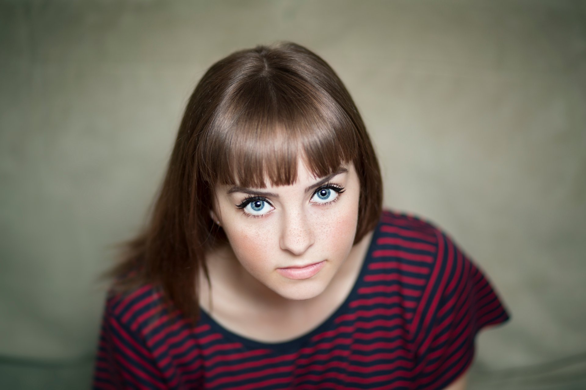 A 4K Ultra HD portrait of a brunette woman with freckles and striking blue eyes, wearing a striped top, looking directly at the camera.