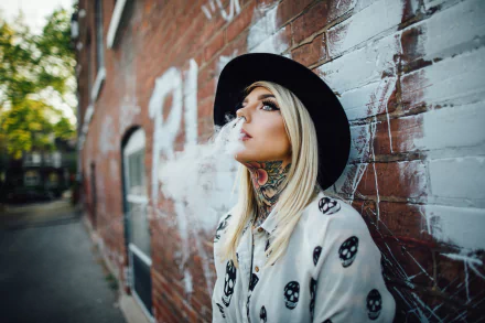 A blonde woman, wearing a hat and tattooed on her neck, smokes against a graffiti-covered brick wall. This HD desktop wallpaper and background creates a bold, urban aesthetic.