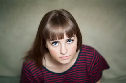 A 4K Ultra HD portrait of a brunette woman with freckles and striking blue eyes, wearing a striped top, looking directly at the camera.