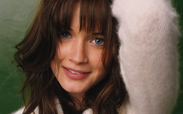 HD desktop wallpaper of a smiling female celebrity — close-up portrait with blue eyes and tousled brown hair, wearing a soft white sweater against a green backdrop.
