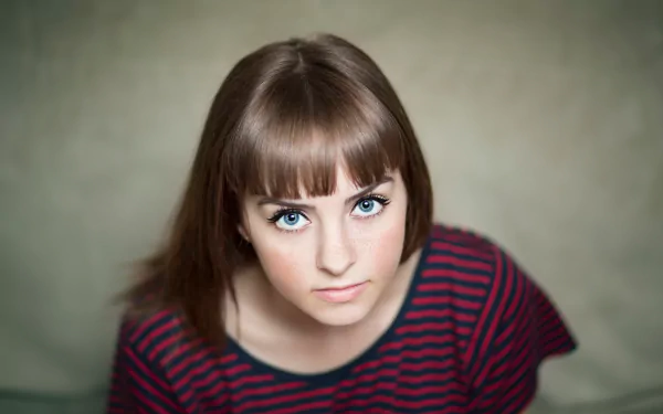 A 4K Ultra HD portrait of a brunette woman with freckles and striking blue eyes, wearing a striped top, looking directly at the camera.