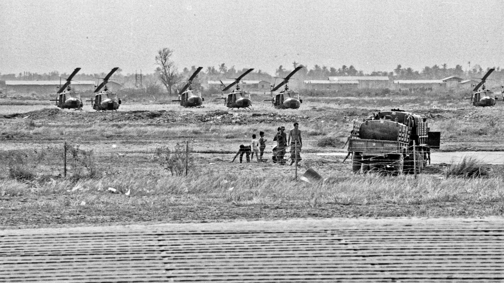 Black-and-white Vietnam War military scene: field artillery lined up, soldiers and a supply truck in foreground — HD PC desktop wallpaper and background.