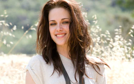 A vibrant HD desktop wallpaper featuring Kristen Stewart smiling outdoors, surrounded by lush greenery, capturing her natural beauty and effortless charm.