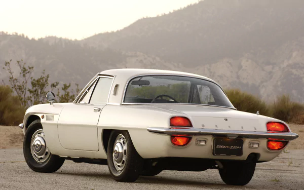 Rear three-quarter view of a white Mazda Cosmo coupe parked on a desert road with mountains — 4K Ultra HD PC desktop wallpaper/background.