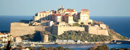Sunlit man-made citadel of Calvi, Haute-Corse: stone ramparts and terracotta roofs on a coastal promontory, HD PC desktop wallpaper and background.