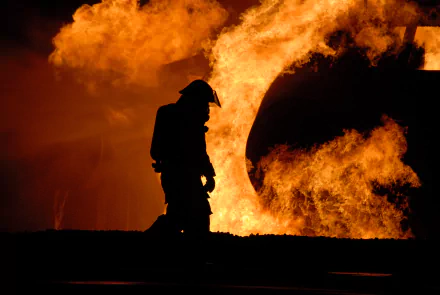 A silhouette of a firefighter stands against a backdrop of intense flames, capturing the bravery and intensity of emergency response. This striking image serves as a dramatic 4K Ultra HD desktop wallpaper.