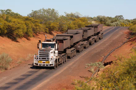 A Kenworth road train drives along a dirt road surrounded by greenery, showcasing heavy vehicle power in a vast landscape, captured in stunning 4K Ultra HD quality.