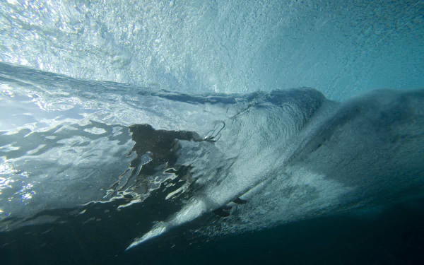 Underwater view of a surfer riding inside a translucent wave barrel with dynamic blue water textures — 2K Quad HD PC desktop wallpaper and background, surfing sports.