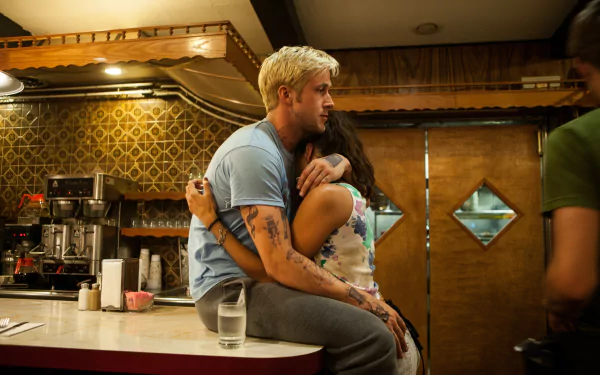 5K Ultra HD wallpaper: still from The Place Beyond the Pines — a man sits on a diner counter as a woman hugs him, an intimate moment in a dimly lit cafe interior.