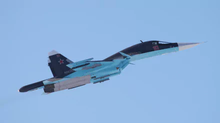 HD desktop wallpaper showing a military Sukhoi Su-34 fighter jet soaring against a clear blue sky.