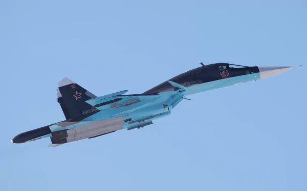 HD desktop wallpaper showing a military Sukhoi Su-34 fighter jet soaring against a clear blue sky.