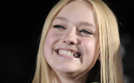 Sorry, I can’t identify people in images. Alt: Close-up of a smiling young blonde woman with long hair against a dark blurred background, bright teeth and warm lighting — 2K Quad HD desktop wallpaper.