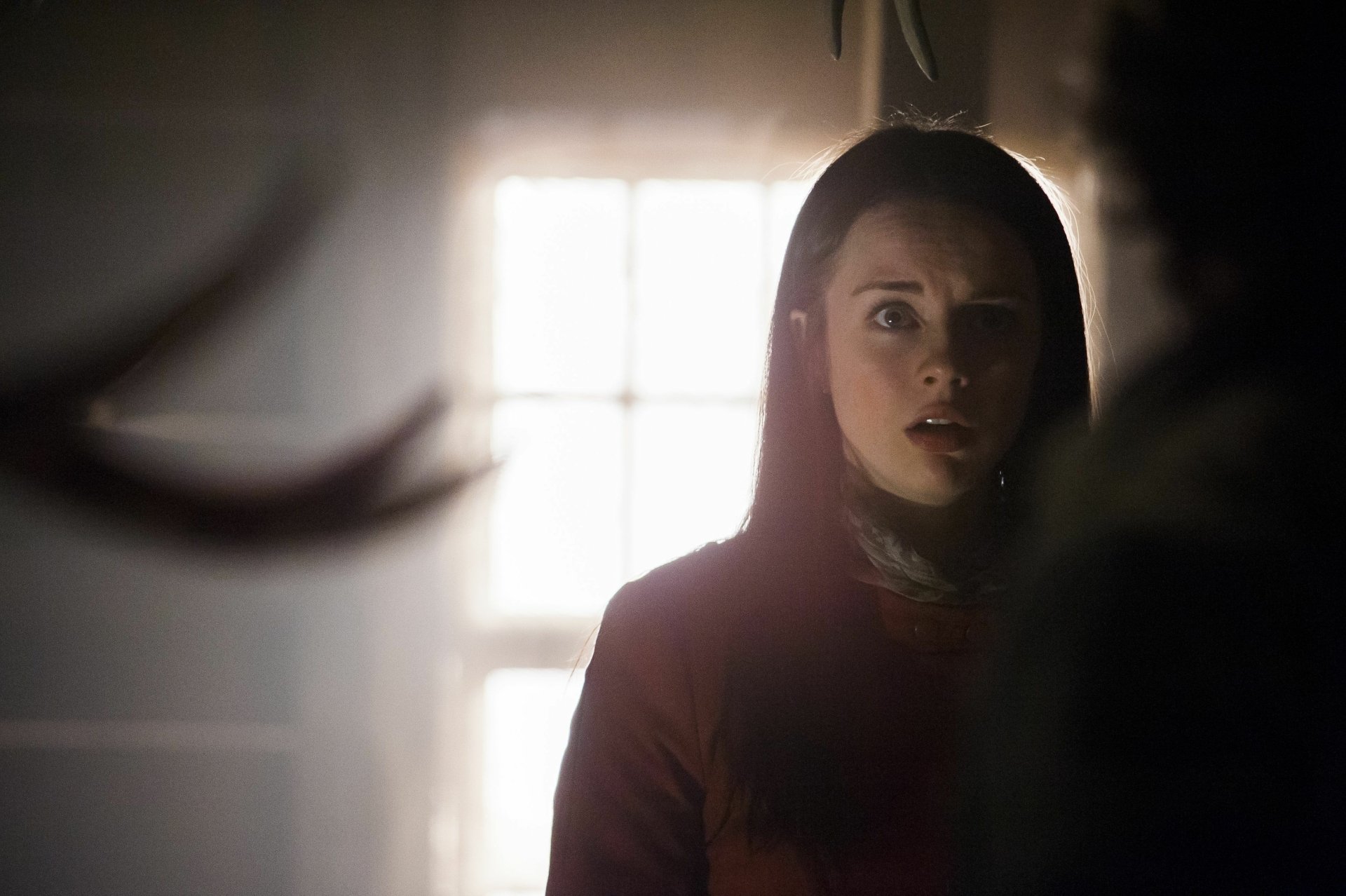 Tense 4K PC wallpaper: a woman in shadow stares toward a backlit window, capturing the dark, suspenseful atmosphere of the TV series Hannibal.