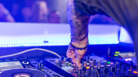 HD PC desktop wallpaper featuring a DJ adjusting controls on a mixing console in a vibrant, blue-lit music environment.
