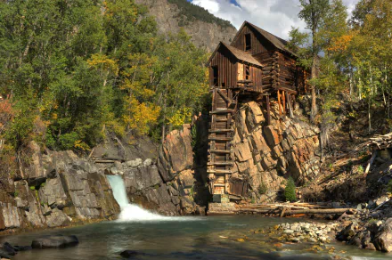 Crystal Mill on a rocky ledge above a rushing stream, framed by autumn trees — 4K Ultra HD man-made historic mill PC desktop wallpaper