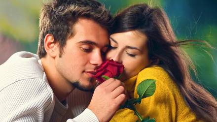 A romantic HD desktop wallpaper of a couple sharing a tender moment, with the man holding a red rose close to them. The background is softly blurred, highlighting their expressions of love and affection.