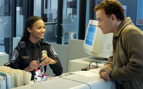 HD desktop wallpaper featuring Zoe Saldana and Tom Hanks in a scene from the movie The Terminal, with Saldana in uniform and Hanks leaning on a counter.