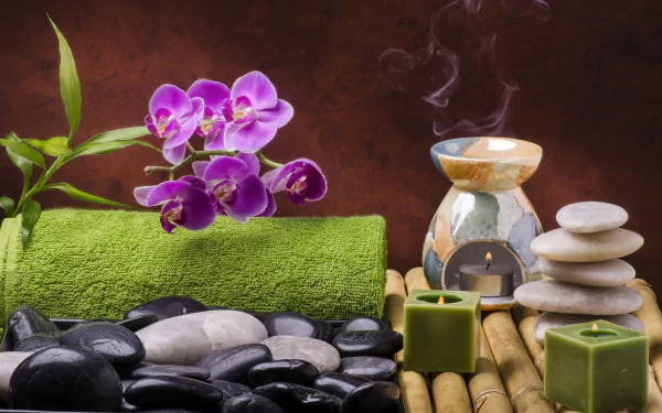 4K Ultra HD still life of a spa scene with vibrant purple orchid, green towel, candle, aromatic oil burner, salt, stacked stones, and smooth black stones on bamboo mat.