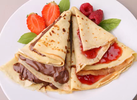 A delicious assortment of crêpes filled with chocolate and jam, garnished with fresh strawberries and raspberries, showcased as a vibrant 4K Ultra HD desktop wallpaper.