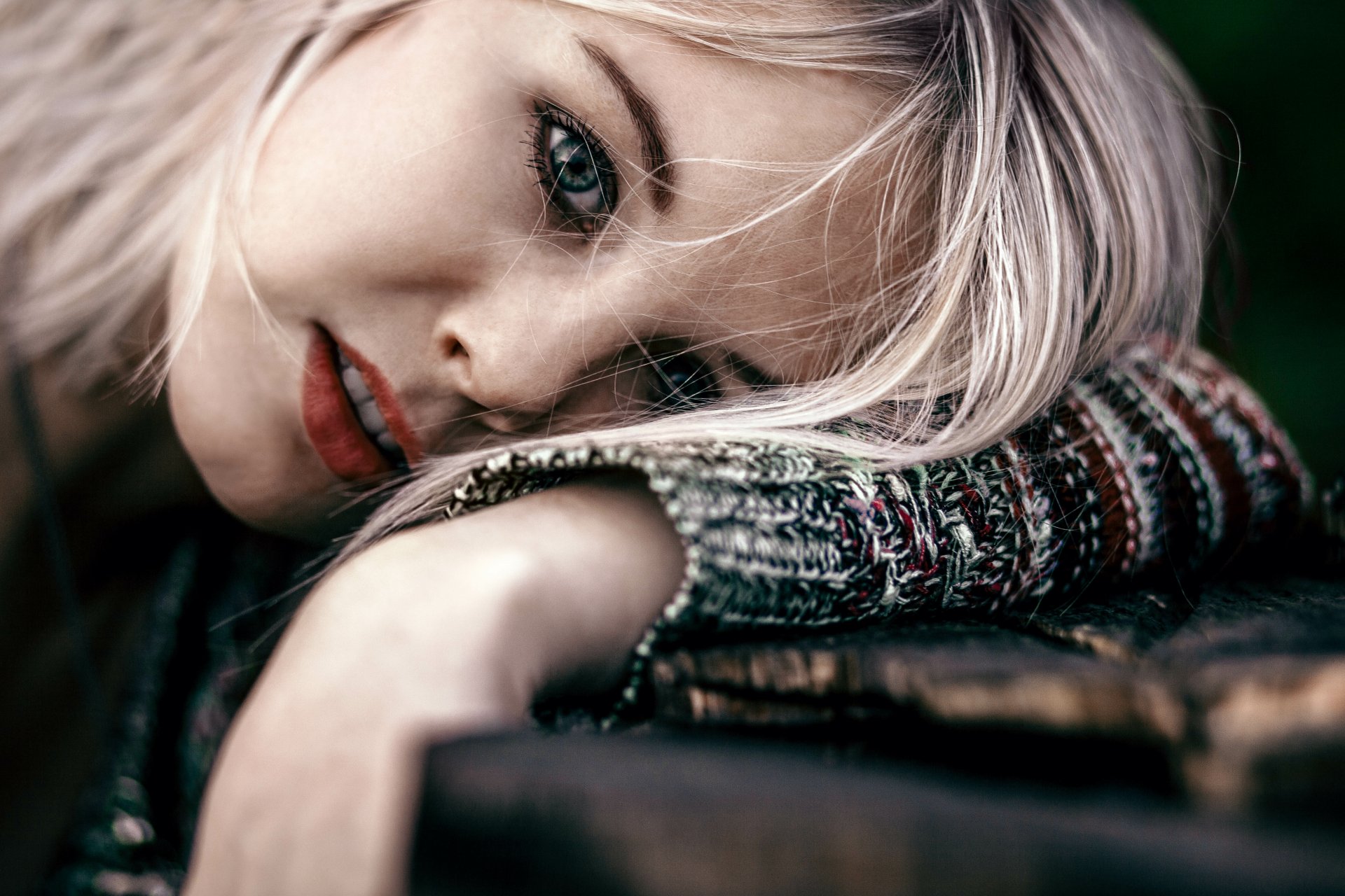 A model with striking green eyes and blonde hair rests her chin on her arm, showcasing her face against a soft, blurred background in this 4K Ultra HD wallpaper.