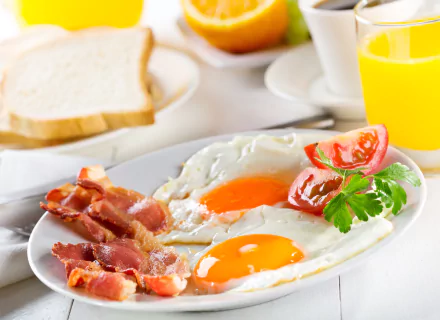 A 4K Ultra HD breakfast featuring sunny-side-up eggs, crispy bacon, tomato slices, toast, and a glass of orange juice.