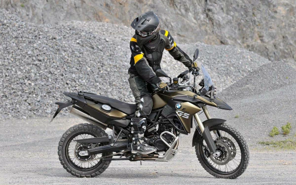 A rider on a BMW F800GS Adventure motorcycle stands on rocky terrain, captured in an HD PC desktop wallpaper featuring the BMW F800GS vehicle.