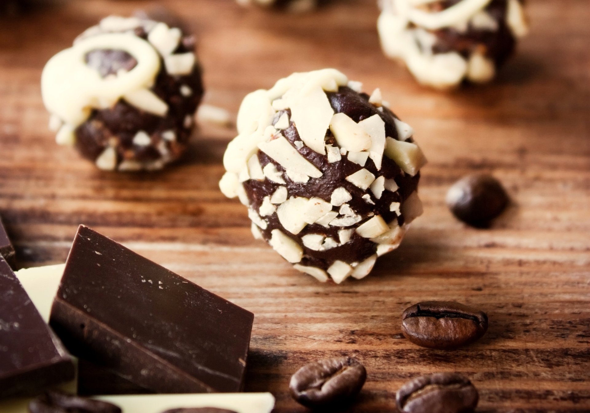 Close-up of chocolate truffles topped with chopped nuts, surrounded by coffee beans and dark chocolate pieces on a wooden surface, captured in HD for a desktop wallpaper.