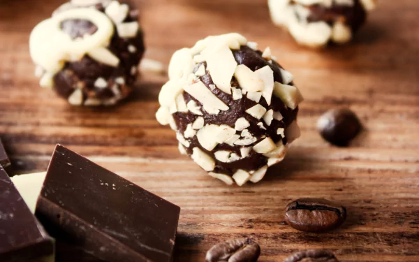 Close-up of chocolate truffles topped with chopped nuts, surrounded by coffee beans and dark chocolate pieces on a wooden surface, captured in HD for a desktop wallpaper.