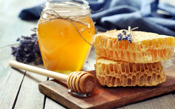 A jar of honey sits beside honeycomb stacks, adorned with lavender, on a wooden board. This vibrant, 8K Ultra HD image captures a delightful food scene.