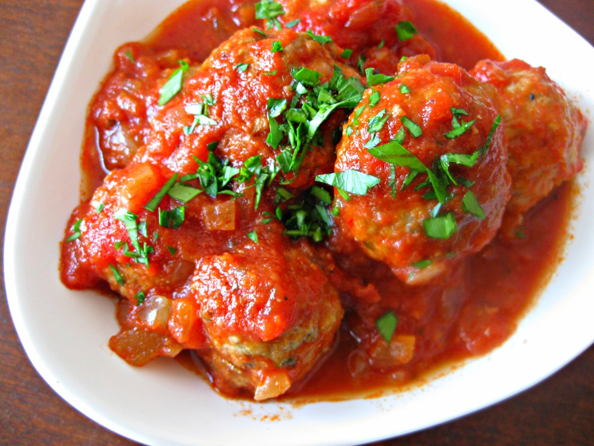 HD PC desktop wallpaper featuring a close-up of juicy meatballs garnished with fresh herbs, bathed in rich red tomato sauce.