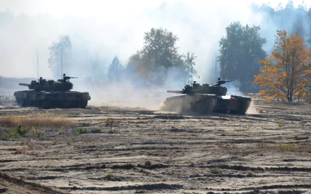 Two PT-91 Twardy tanks advancing across a dusty terrain in a military exercise, captured in high-definition detail for a PC desktop wallpaper.