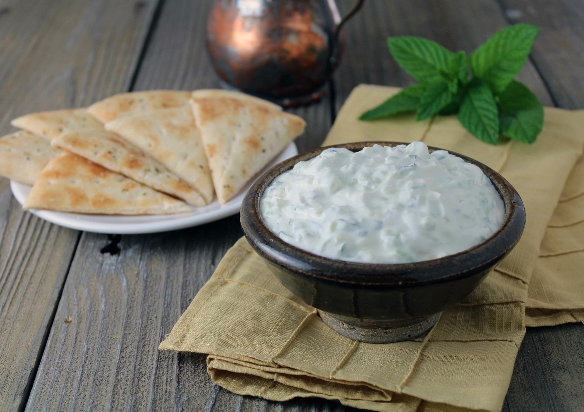 A bowl of creamy tzatziki sauce with sliced pita bread on a plate, set on a wooden table, captured in 4K Ultra HD as a PC desktop wallpaper and background.