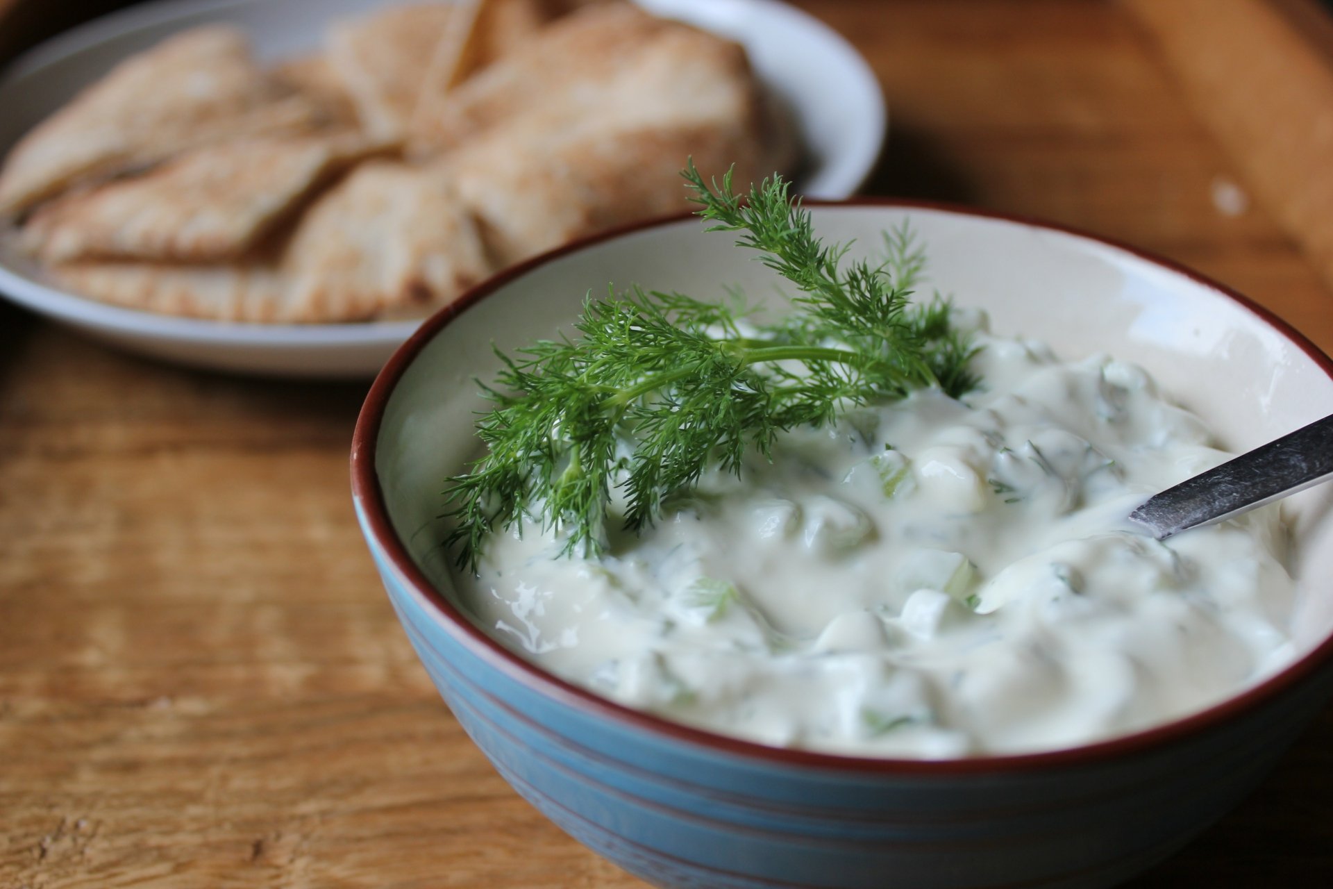 Close-up of a bowl of creamy tzatziki garnished with dill, accompanied by pita bread, captured as a vibrant 4K Ultra HD PC desktop wallpaper.
