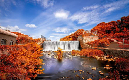 HD desktop wallpaper featuring a man-made dam surrounded by vibrant orange foliage under a bright blue sky.