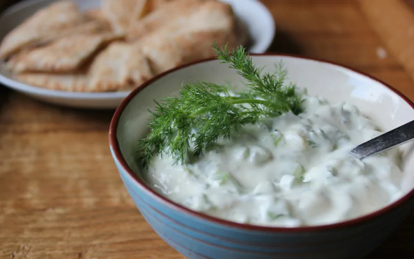 Close-up of a bowl of creamy tzatziki garnished with dill, accompanied by pita bread, captured as a vibrant 4K Ultra HD PC desktop wallpaper.