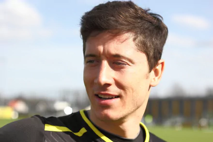 HD desktop wallpaper of Polish soccer player Robert Lewandowski, sporting a black and yellow training jersey, with a blurred outdoor background and a clear blue sky.