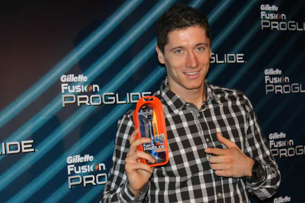 Robert Lewandowski holding a Gillette Fusion ProGlide razor in front of an advertising backdrop. The HD desktop wallpaper captures the Polish soccer star in a casual checkered shirt, smiling.