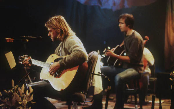 A high-definition desktop wallpaper featuring musicians from Nirvana performing acoustically, capturing an intimate moment on stage with guitars and a soft, moody background.