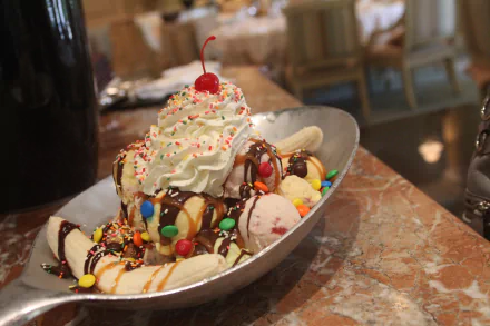HD desktop wallpaper of a colorful banana split topped with whipped cream, a cherry, sprinkles, and drizzled chocolate sauce.