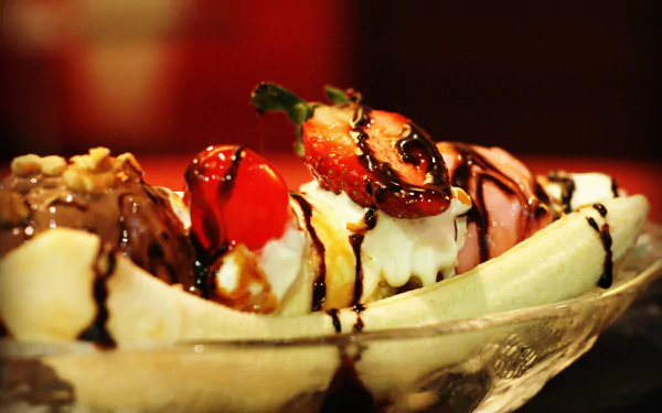 HD desktop wallpaper featuring a close-up of a banana split dessert with ice cream, strawberries, cherries, nuts, and chocolate drizzle.