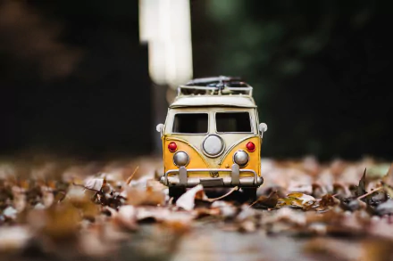A vibrant yellow Volkswagen van toy sits amid colorful fall leaves, showcasing a playful blend of nostalgia and seasonal charm in this HD desktop wallpaper.