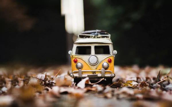 A vibrant yellow Volkswagen van toy sits amid colorful fall leaves, showcasing a playful blend of nostalgia and seasonal charm in this HD desktop wallpaper.