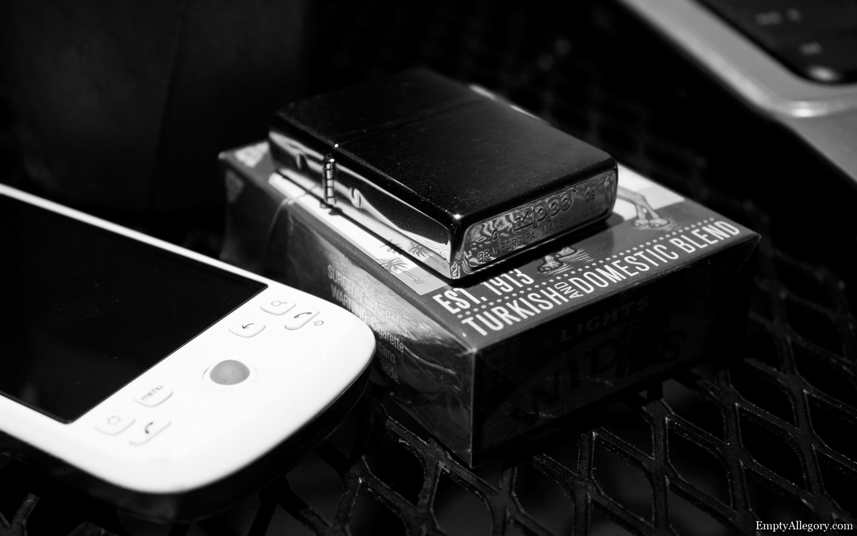 Black and white still life photo showing a lighter resting on a cigarette pack next to a gaming device, captured in close-up as an HD desktop wallpaper.
