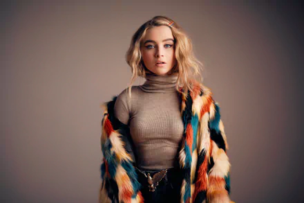 A striking HD wallpaper featuring American singer Sabrina Carpenter, showcasing her blue eyes and blonde hair, styled in a colorful fur coat against a neutral background.