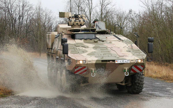 4K Ultra HD PC desktop wallpaper of a camouflaged military armored personnel carrier splashing through mud on a forest road.