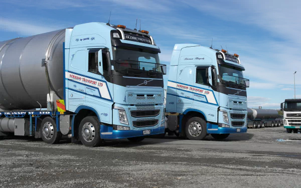 5K Ultra HD PC desktop wallpaper showing two light-blue Volvo tanker trucks parked on gravel under a crisp blue sky