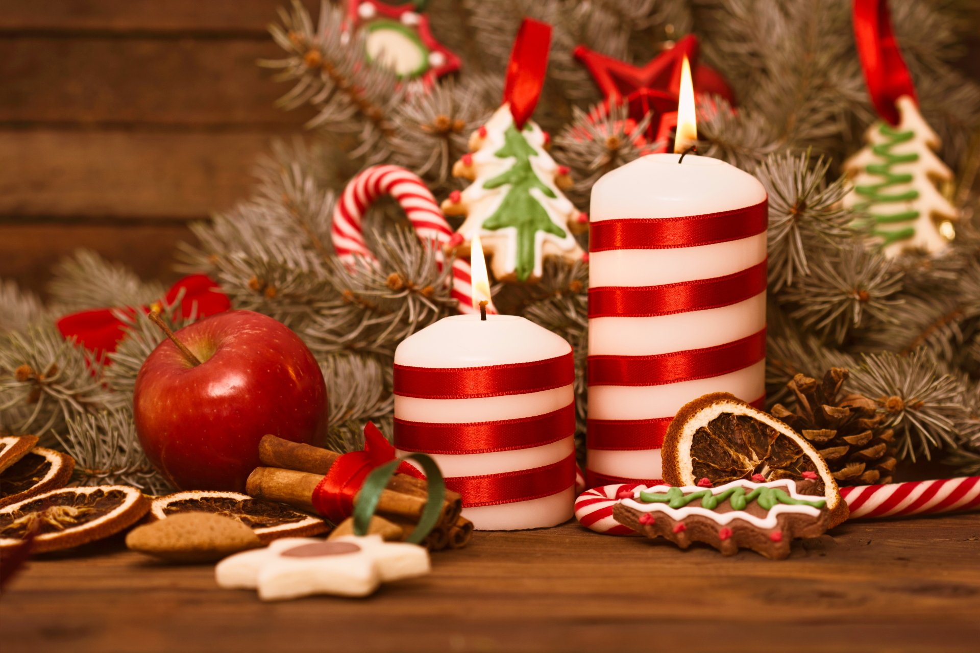 Festive Christmas scene with cinnamon sticks, apple, striped candles, gingerbread cookie, candy canes, and holiday ornaments on a rustic wooden table in 4K Ultra HD.