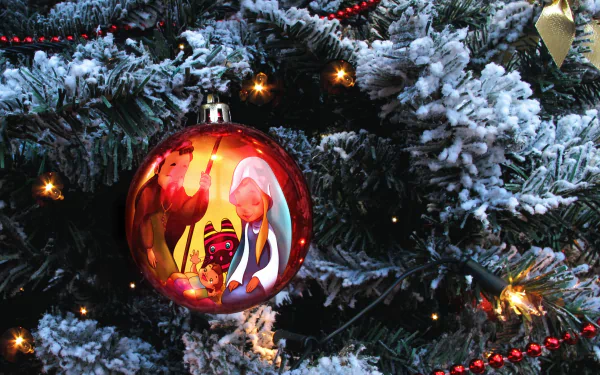 Nativity-themed Christmas ornament on a snow-dusted fir tree with glowing lights and red beads — holiday 2K Quad HD PC desktop wallpaper and background.