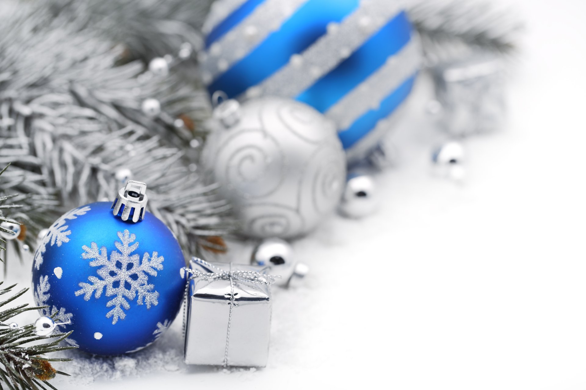A 4K Ultra HD Christmas desktop wallpaper featuring blue and silver holiday ornaments and a small wrapped gift on frosted pine branches.